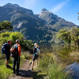 Walkers pause beside Lake Ada with dramatic mountain peaks towering in the distance.
