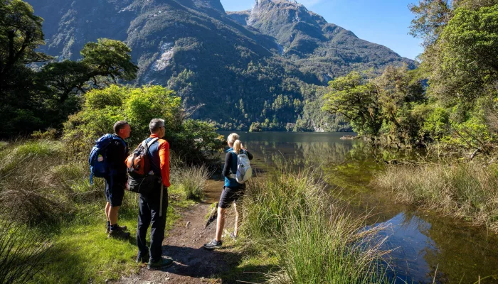 Walkers pause beside Lake Ada with dramatic mountain peaks towering in the distance.
