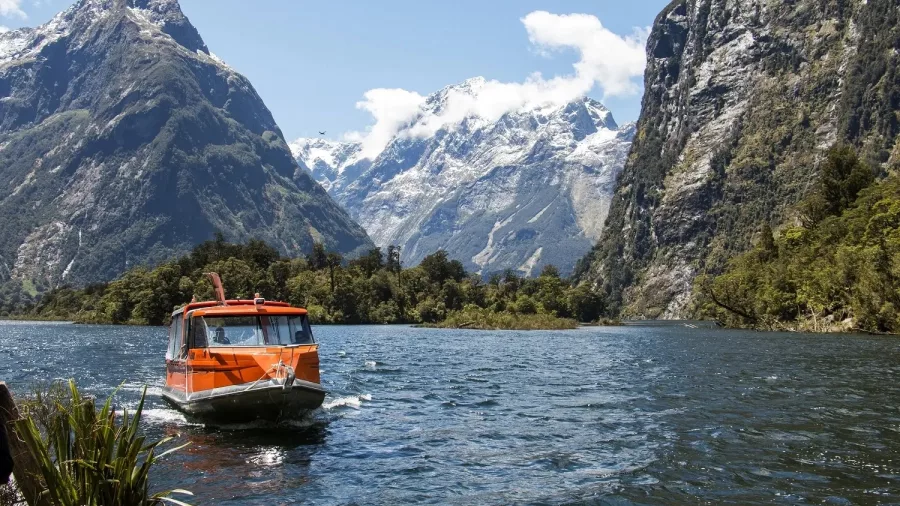 Water taxi arrives at Sandfly Point with snow-capped peaks rising behind in Milford Sound.