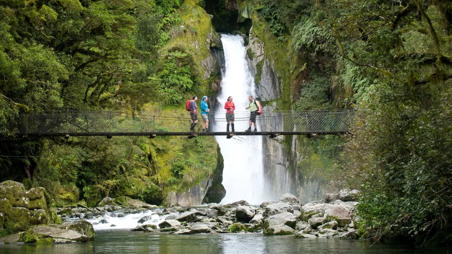 Group of hikers standing on the swing bridge in front of Giant Gate Falls on the Milford Track.