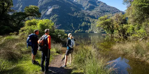 Walkers pause beside Lake Ada with dramatic mountain peaks towering in the distance.