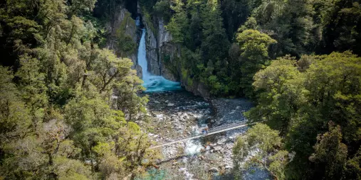 Aerial view of Giant Gate Waterfall and suspension bridge framed by lush Fiordland forest.