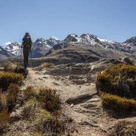 Solo hiker standing at Key Summit on the Routeburn Track with panoramic mountain views.