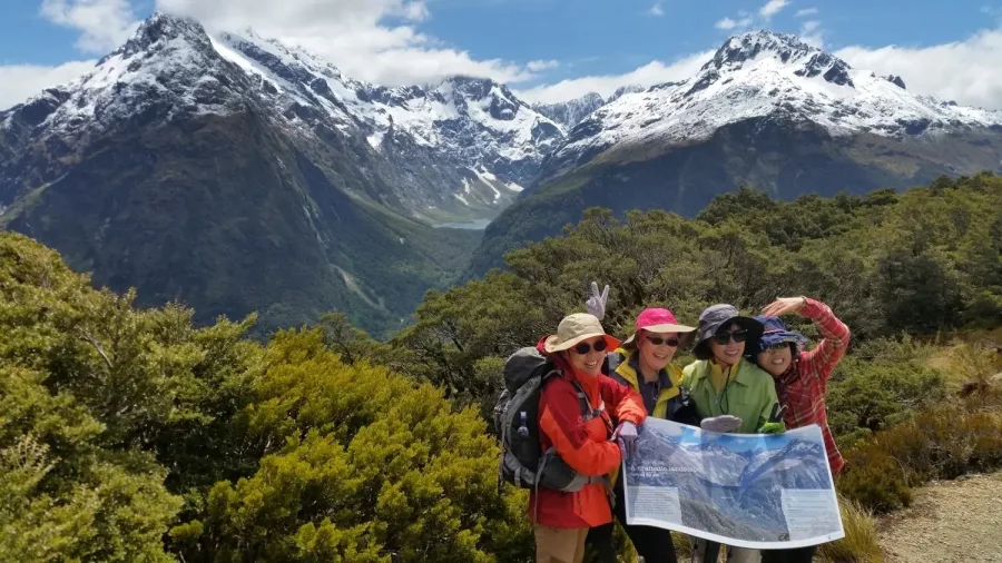 Group of friends checking a map with snowy mountains in the background.