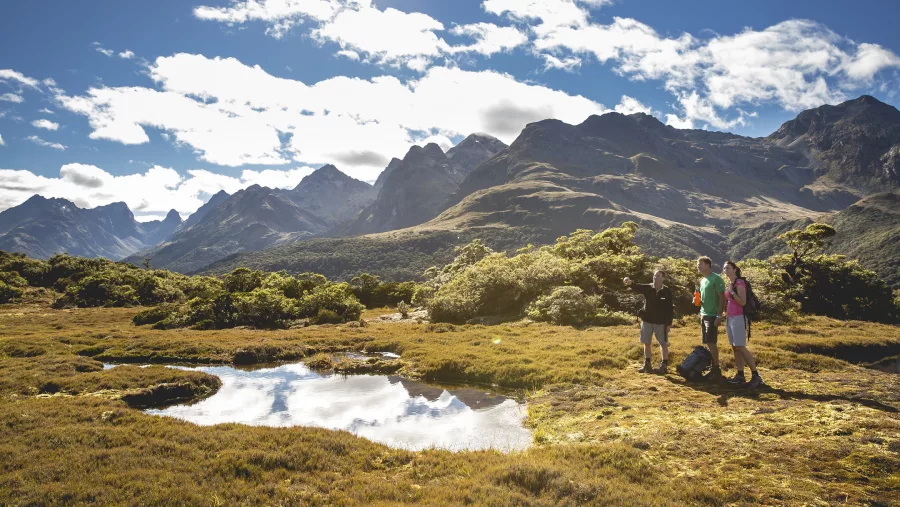 Small reflective alpine tarn at Key Summit with hikers nearby on the Routeburn Track.