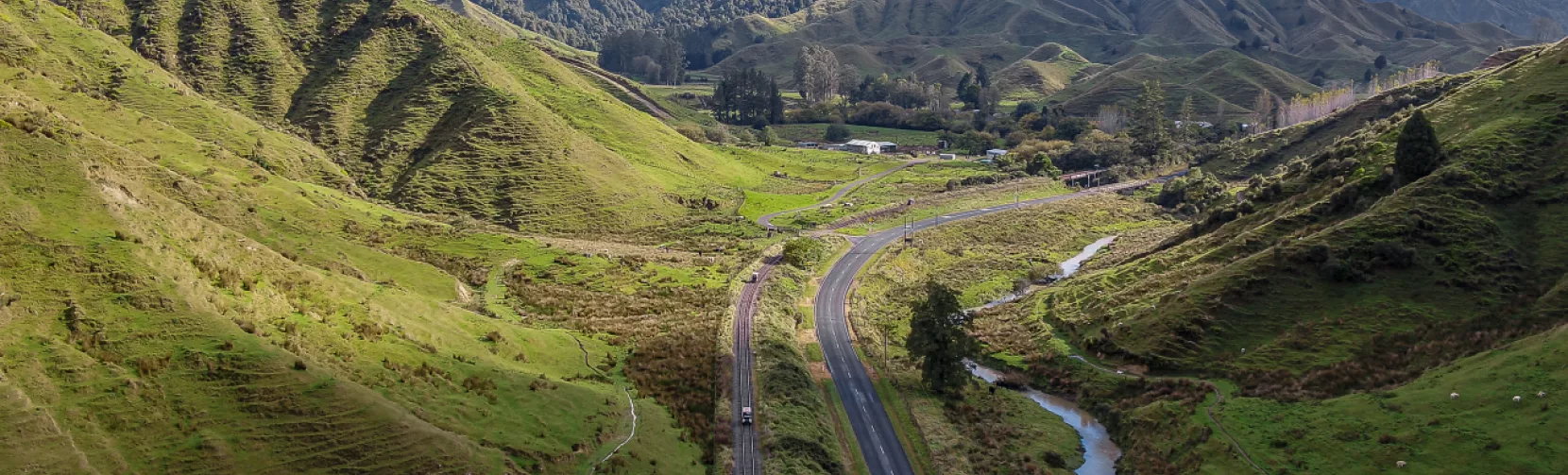 Aerial view of rail line and road winding through lush valleys on the Forgotten World Highway
