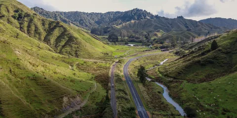 Aerial view of rail line and road winding through lush valleys on the Forgotten World Highway