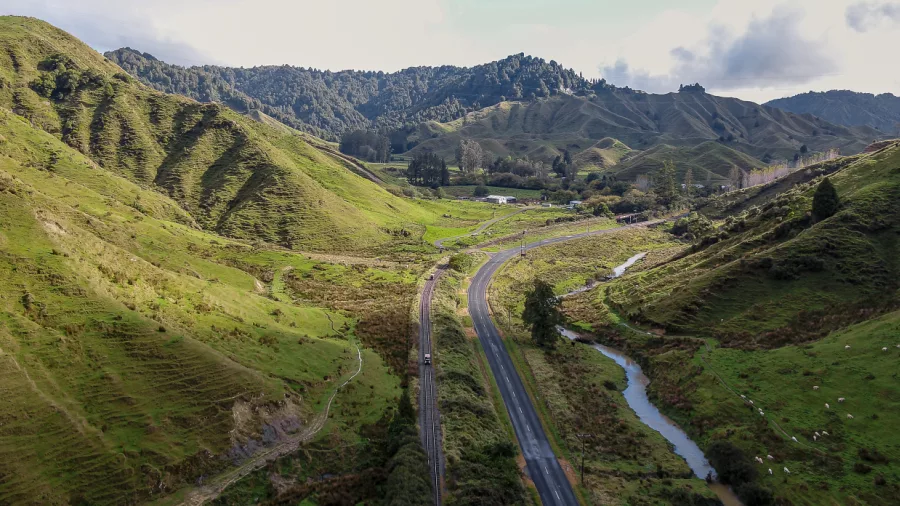 Aerial view of rail line and road winding through lush valleys on the Forgotten World Highway