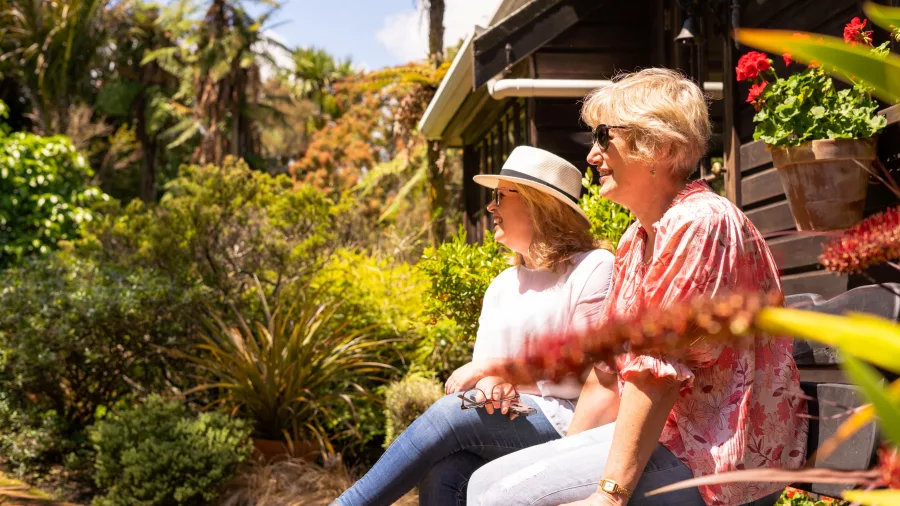 Two women relaxing in the sun at Te Kainga Marire garden in Taranaki