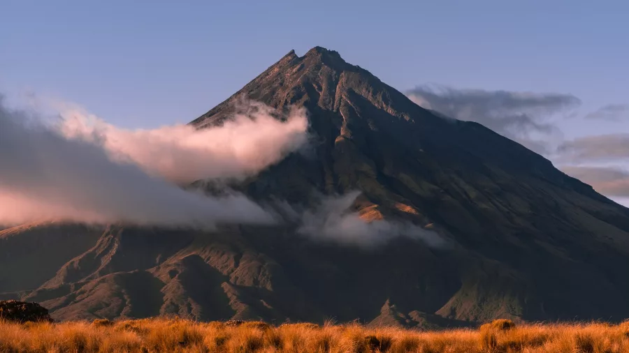 Cloudy view of Mount Taranaki at sunrise reflected in Pouākai Tarn in Egmont National Park