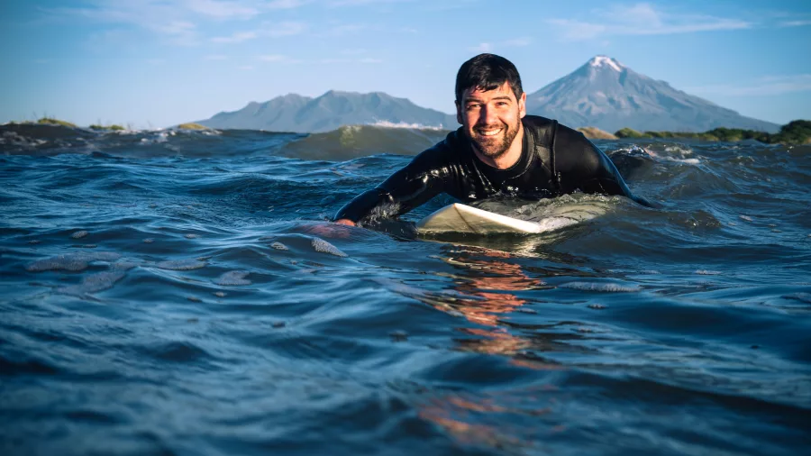 Surfer paddling out at Rocky Rights in New Plymouth with Mount Taranaki in the background