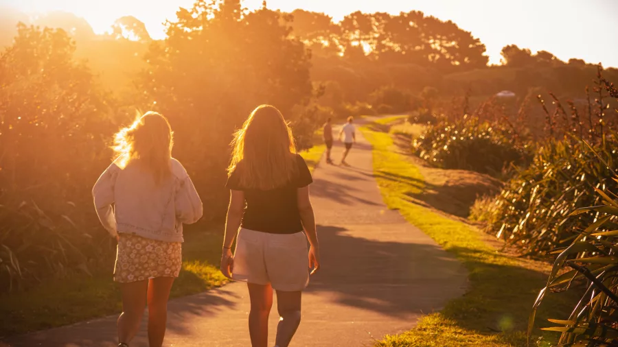 Two women walking the Coastal Walkway in New Plymouth during golden hour