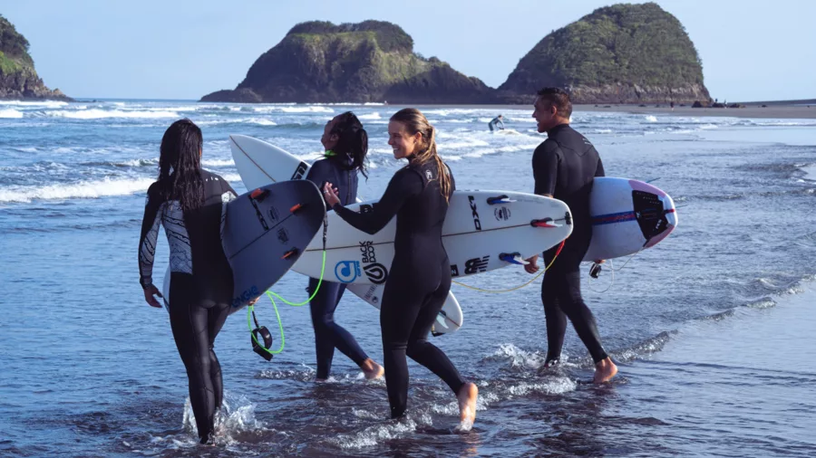 Group of surfers walking along the shore at Back Beach, New Plymouth with surfboards and island backdrop