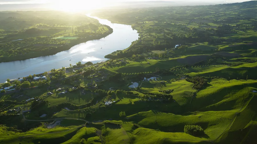 Aerial view of Lake Karapiro near Cambridge in the Waikato region, showcasing the winding waterway, rolling green hills, and surrounding farmland at sunrise.