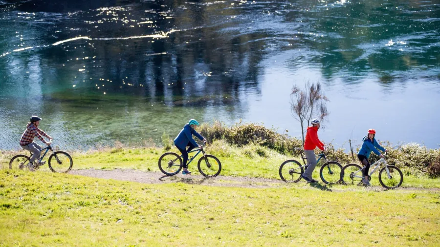 Four cyclists riding single file along the Waikato River Trail near Taupō