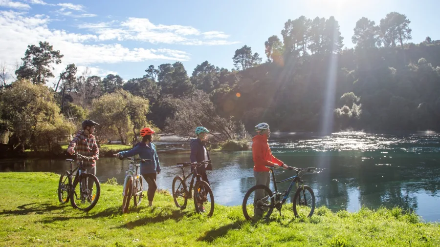 Group of cyclists pausing beside the Waikato River near Taupō Bungy on a sunny day