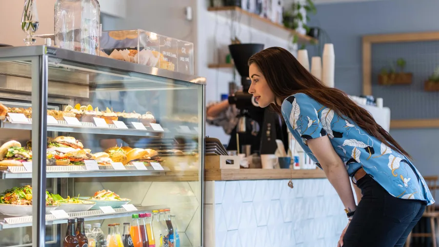 Woman leaning over a glass display case to choose from fresh bakery items at a café in Hamilton, Waikato.