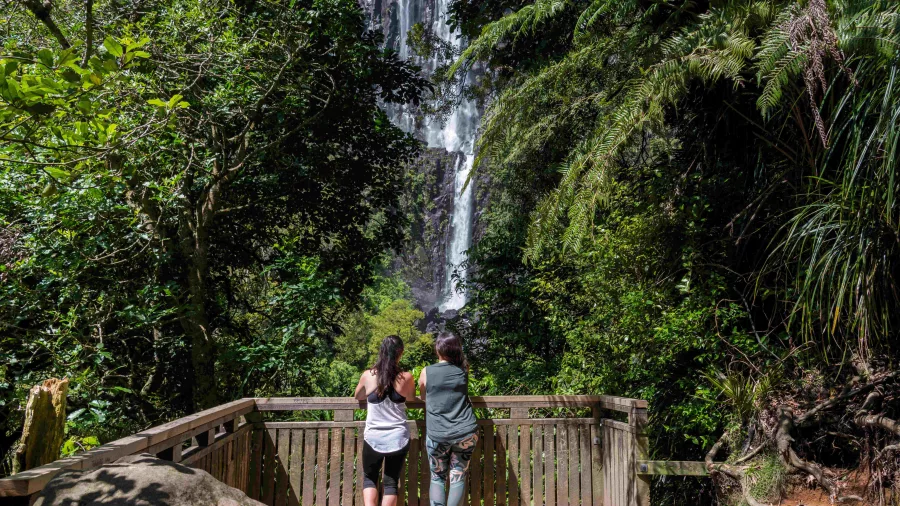 Two women standing at the Wairere Falls lower lookout platform surrounded by native bush in the Kaimai Ranges near Matamata