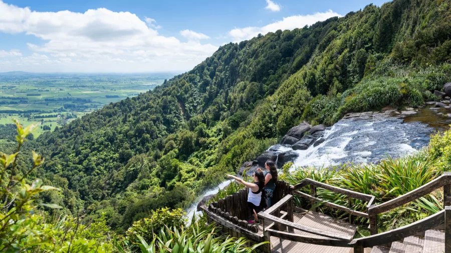 Walkers standing at the top lookout of Wairere Falls with panoramic views over Waikato farmland and bush-clad hills