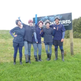 Group of smiling guests in caving gear posing at the Glowing Adventures sign before a private Waitomo tour