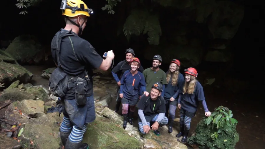Tour guide taking a group photo of smiling guests at a cave entrance during a Glowing Adventures private tour in Waitomo