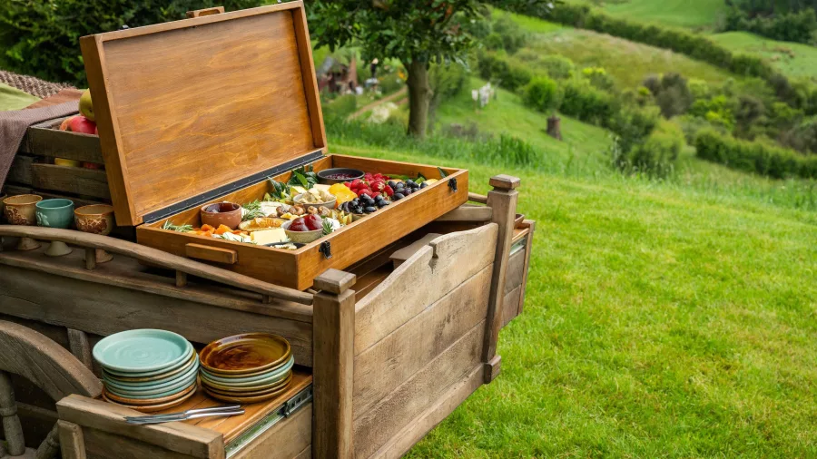 Wooden cart filled with a picnic box of cheeses, fruits, and snacks overlooking the Hobbiton hills