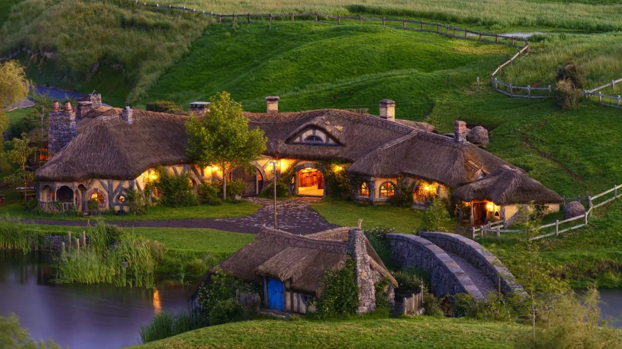 Green Dragon Inn at Hobbiton Movie Set lit up at dusk with a stone bridge and grass-covered roofs