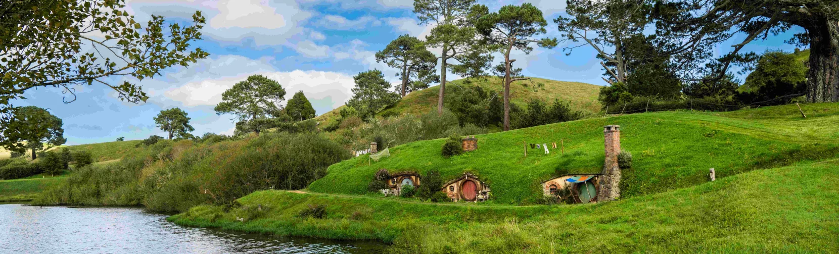 Lush green hills and Hobbit holes set along a peaceful lakefront at the Hobbiton Movie Set in New Zealand