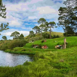 Lush green hills and Hobbit holes set along a peaceful lakefront at the Hobbiton Movie Set in New Zealand