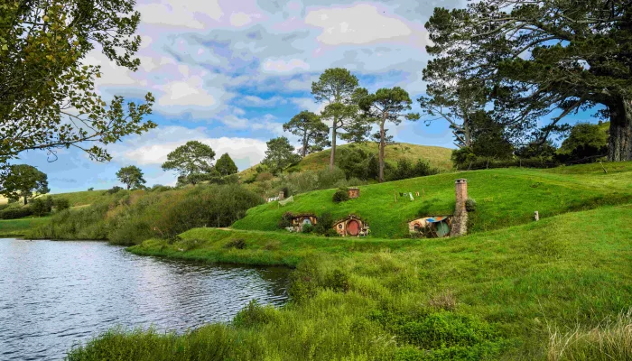 Lush green hills and Hobbit holes set along a peaceful lakefront at the Hobbiton Movie Set in New Zealand