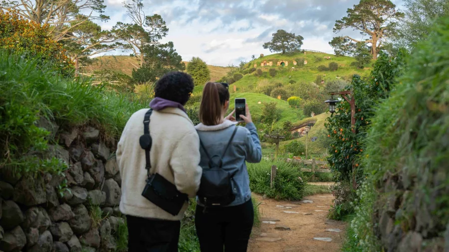Couple taking a photo of Hobbit Holes on a grassy hillside at Hobbiton