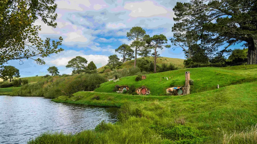 Lush green hills and Hobbit holes set along a peaceful lakefront at the Hobbiton Movie Set in New Zealand