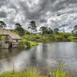 Thatched mill building beside the lake at Hobbiton Movie Set, with trees reflected in the still water
