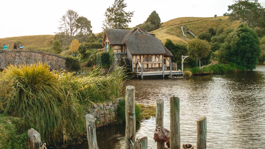 Rustic wooden jetty beside the lake at Hobbiton Movie Set with the watermill and green hills in the background