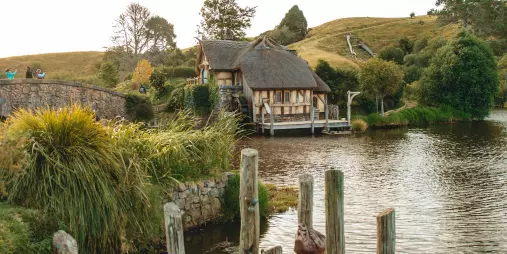 Rustic wooden jetty beside the lake at Hobbiton Movie Set with the watermill and green hills in the background