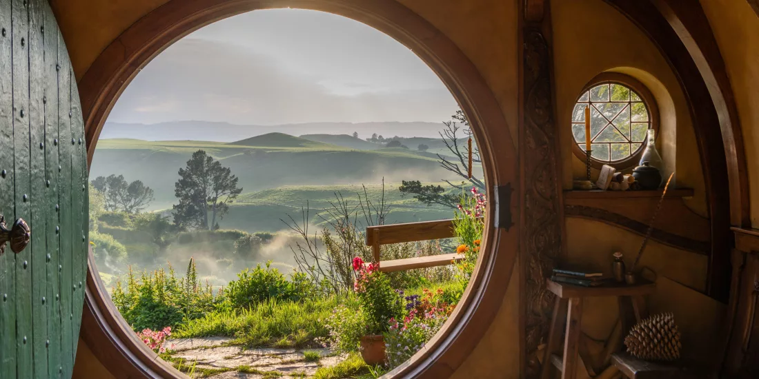 Iconic round doorway view from inside Bag End, looking out to misty hills and garden paths in Hobbiton, New Zealand