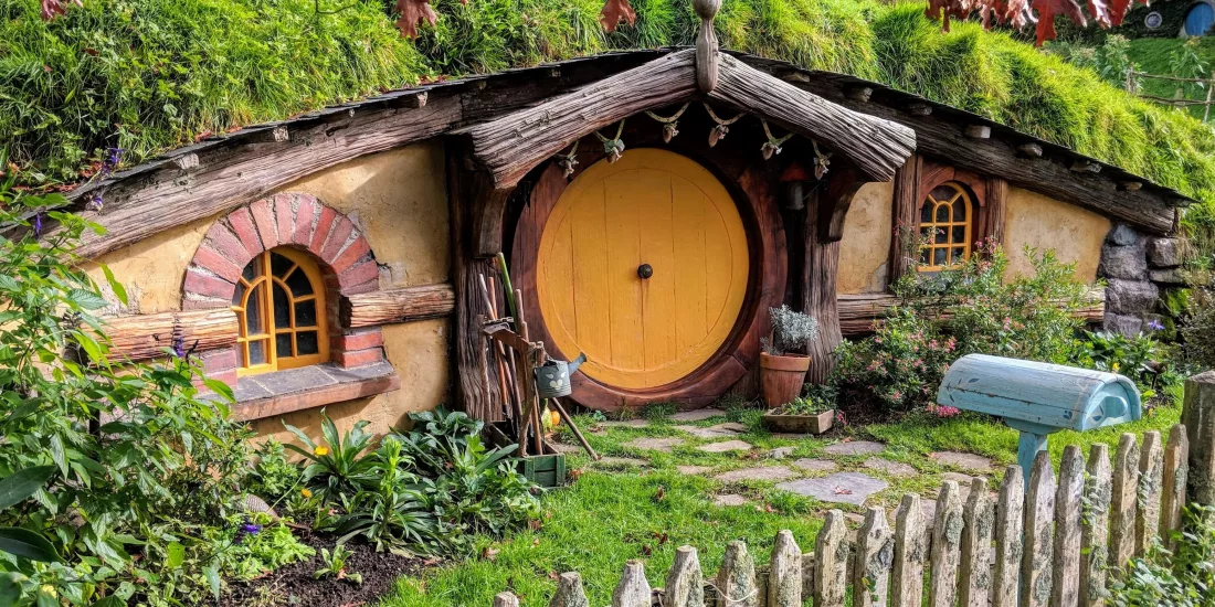 Hobbit house with a yellow round door, rustic garden, and wooden picket fence at the Hobbiton Movie Set