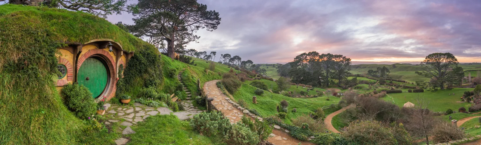 Bag End at the Hobbiton Movie Set in Matamata, with rolling green hills and pathways at sunrise in the Waikato region of New Zealand