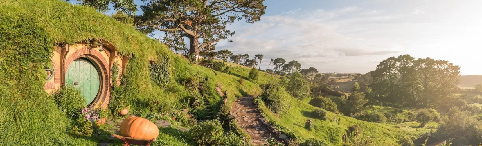 Hobbit holes on a grassy hillside path bathed in soft sunset light at the Hobbiton Movie Set in Waikato
