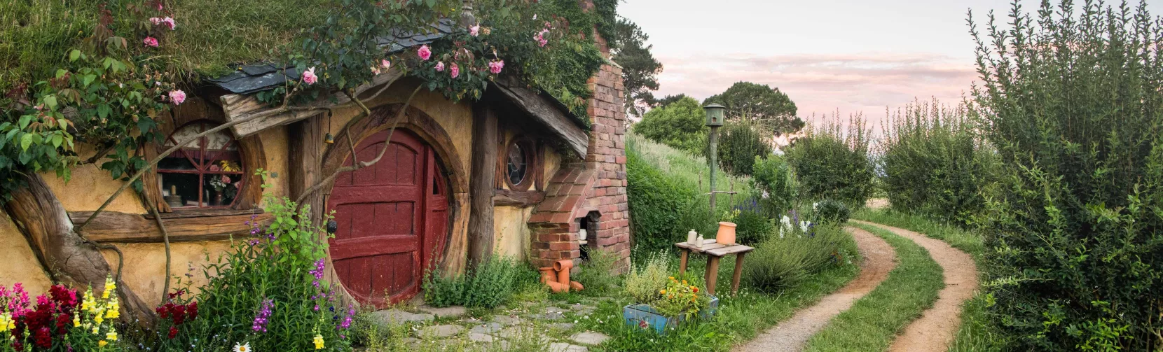 Traditional hobbit house with a red door beside a winding dirt path at the Hobbiton Movie Set near Matamata