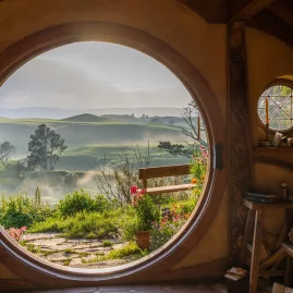Iconic round doorway view from inside Bag End, looking out to misty hills and garden paths in Hobbiton, New Zealand