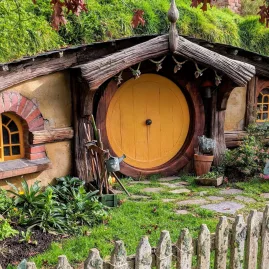 Hobbit house with a yellow round door, rustic garden, and wooden picket fence at the Hobbiton Movie Set