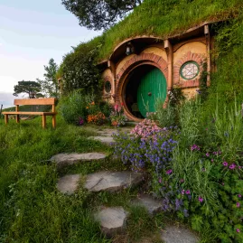 A round green door set into a hillside with flowering plants and a stone path at the Hobbiton Movie Set