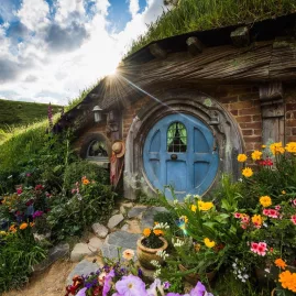 Charming Hobbit hole with a blue round door surrounded by colourful flowers at Hobbiton Movie Set, New Zealand