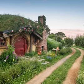 Traditional hobbit house with a red door beside a winding dirt path at the Hobbiton Movie Set near Matamata