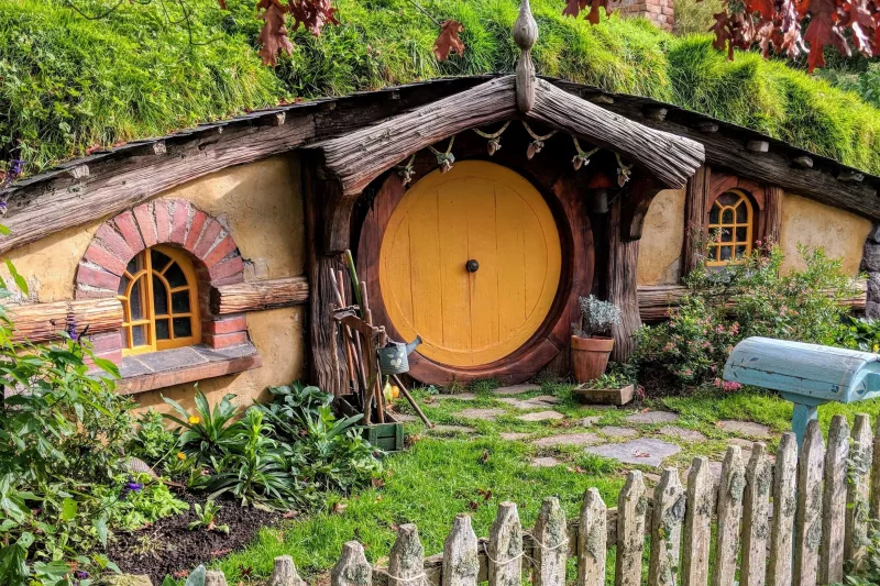 Hobbit house with a yellow round door, rustic garden, and wooden picket fence at the Hobbiton Movie Set