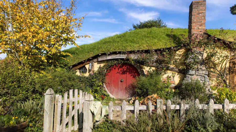Red door hobbit house at Hobbiton Movie Set surrounded by garden and autumn leaves in Matamata New Zealand
