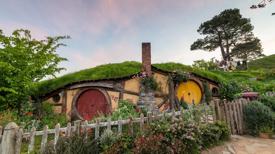 Hobbit holes with red and yellow doors surrounded by vibrant gardens at Hobbiton