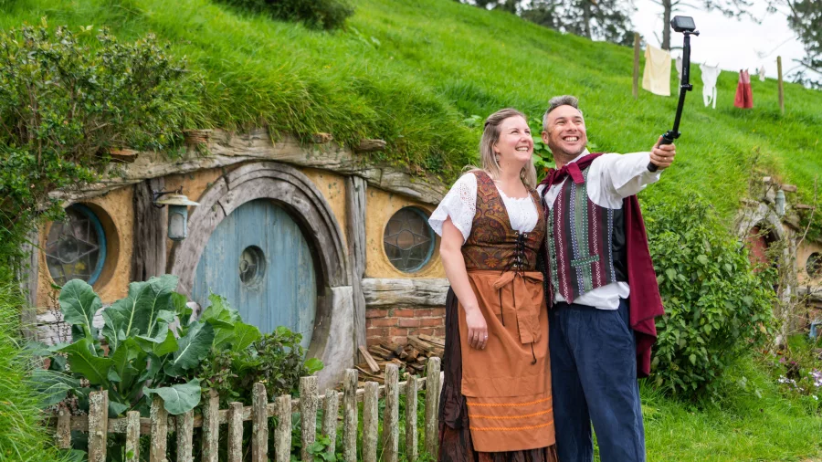 Couple dressed in Hobbit costumes taking a selfie in front of a round Hobbit door