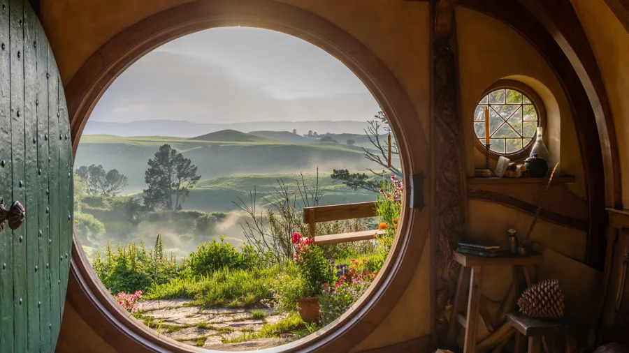 Iconic round doorway view from inside Bag End, looking out to misty hills and garden paths in Hobbiton, New Zealand